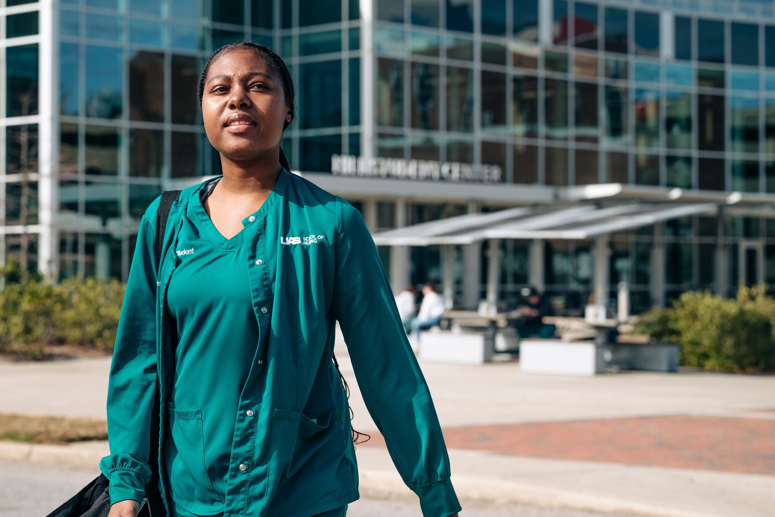 Spring 2025 First Week of Classes. A nursing student
is wearing green scrubs while walking on crosswalk with the Hill Student Center blurred in the background, January 2025.
